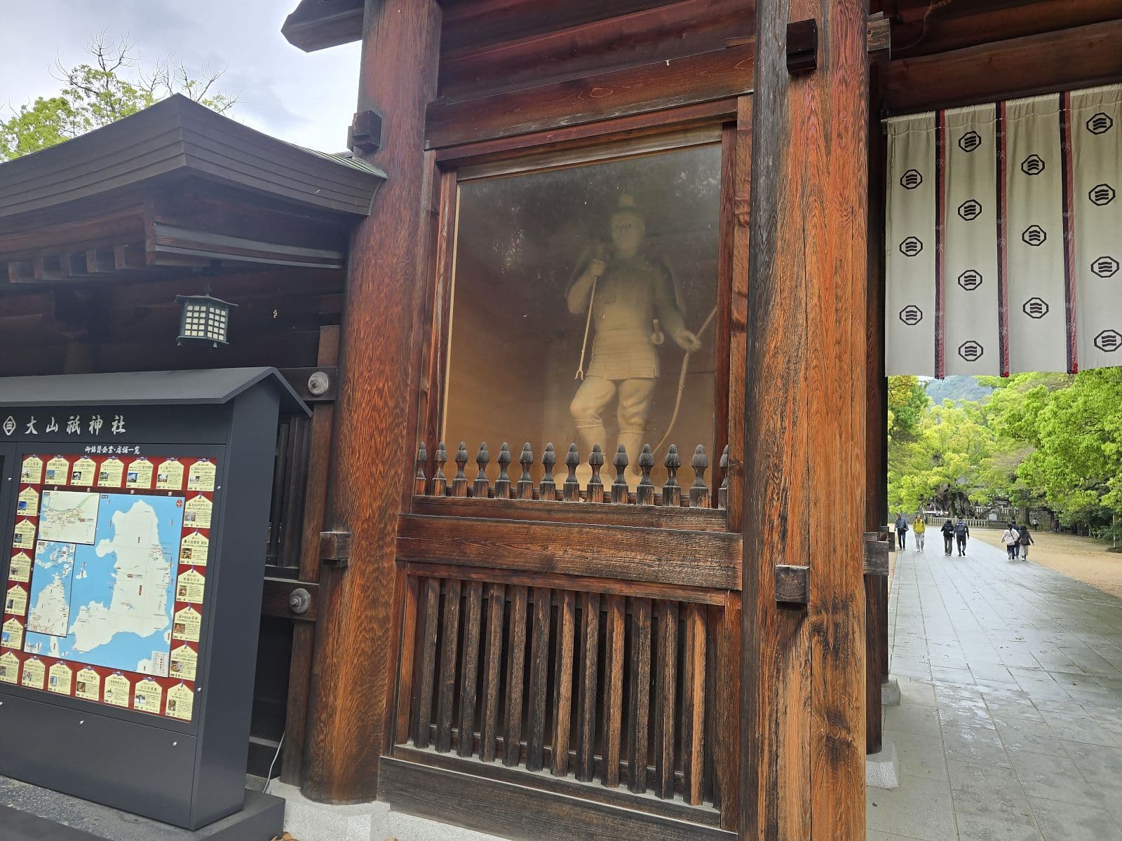 大山祇神社の総門（楼門）柱間に展示された甲冑武将の木製像。ガラスケースに納められている