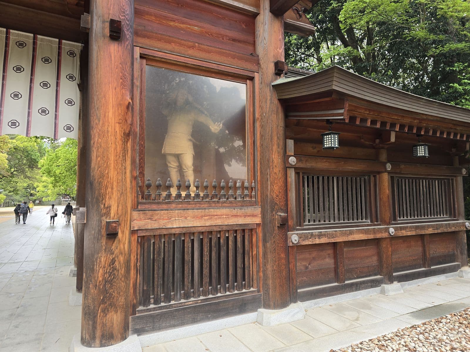 大山祇神社の総門（楼門）柱間に展示された甲冑武将の木製像（右側）。ガラスケースと案内板が見える