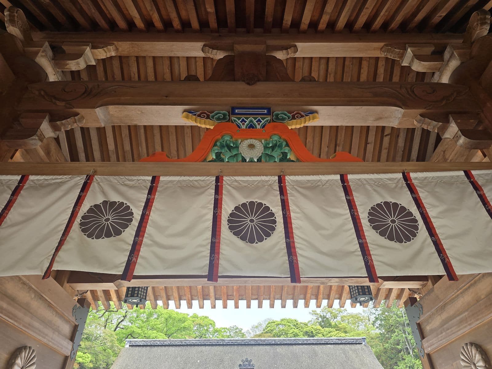 大山祇神社の神門を内側から見上げた天井装飾。朱・青・緑の彫刻と家紋をあしらった白い幕