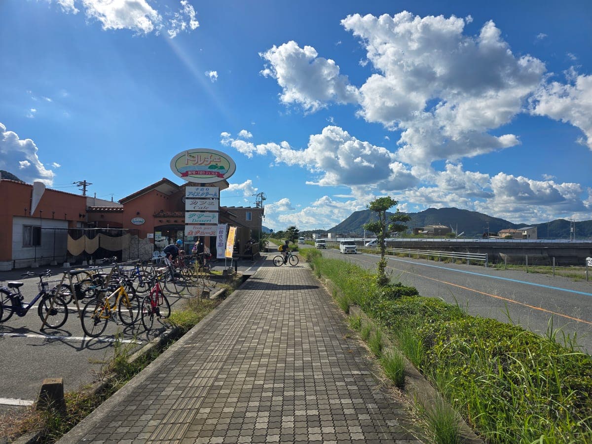生口島・ドルチェの看板と店前に並ぶ自転車(ブロック舗装の歩道から西向き)