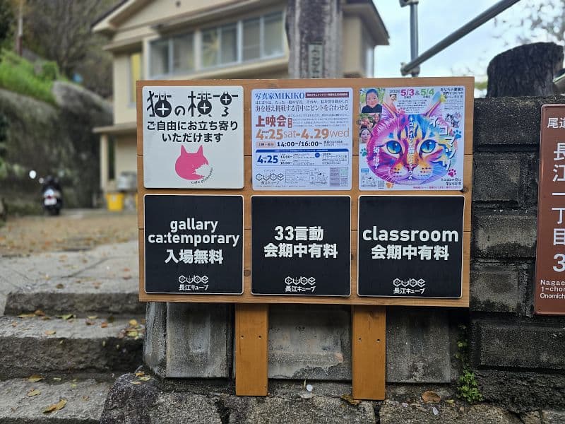 猫の横丁の敷地入口看板——「ご自由にお立ち寄りください」の案内とイベント告知ポスターが貼られている